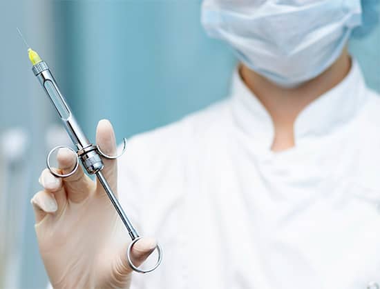 Surgeon holding a syringe for anesthesia administration in facial plastic surgery procedures.