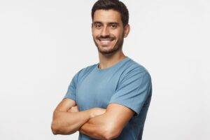 Smiling man in a blue shirt with arms crossed, representing confidence after male breast reduction surgery.