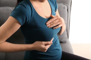 Woman gently holding her breast, illustrating concerns about the effects of pregnancy on breast implants.