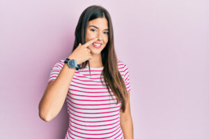 Smiling teenage girl pointing to her nose, representing discussion on appropriate age for rhinoplasty
