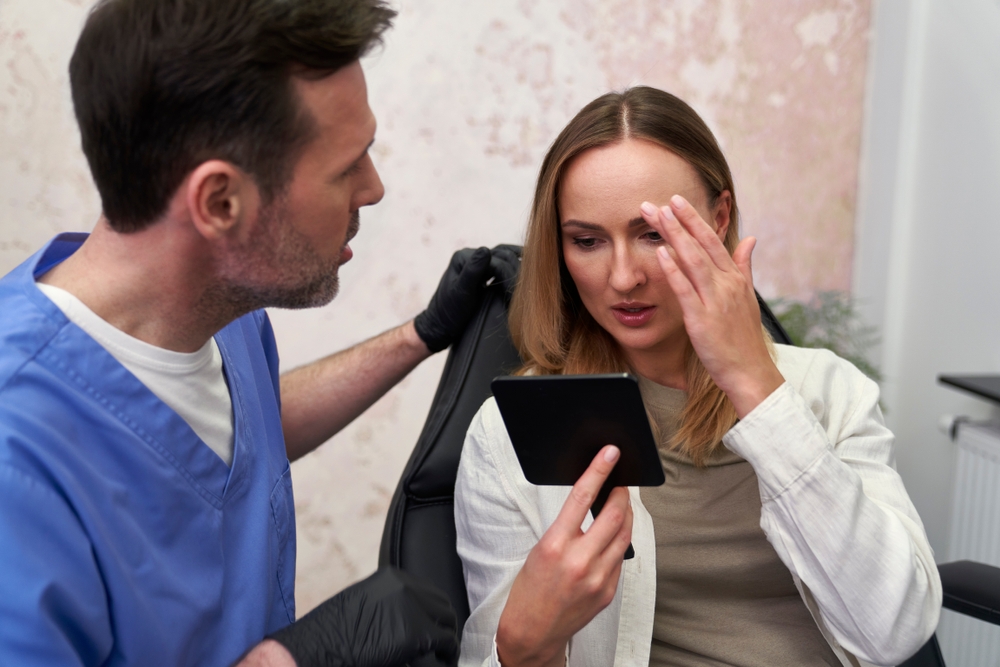 Woman consulting with plastic surgeon while examining her face in mirror before facelift surgery.