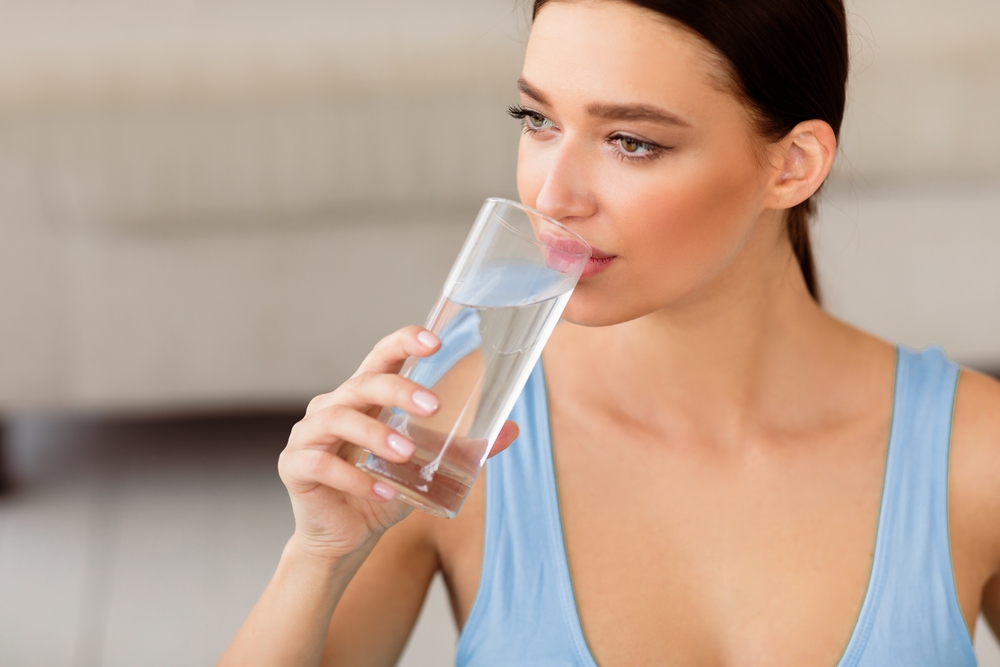 Woman drinking a glass of water, emphasizing the importance of hydration and nutrition before facelift surgery.
