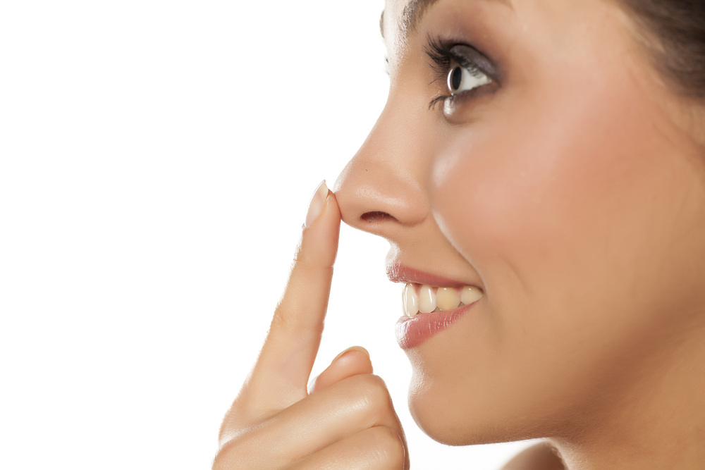Woman smiling in profile, touching nose tip gently, illustrating rhinoplasty healing and nasal tip changes.