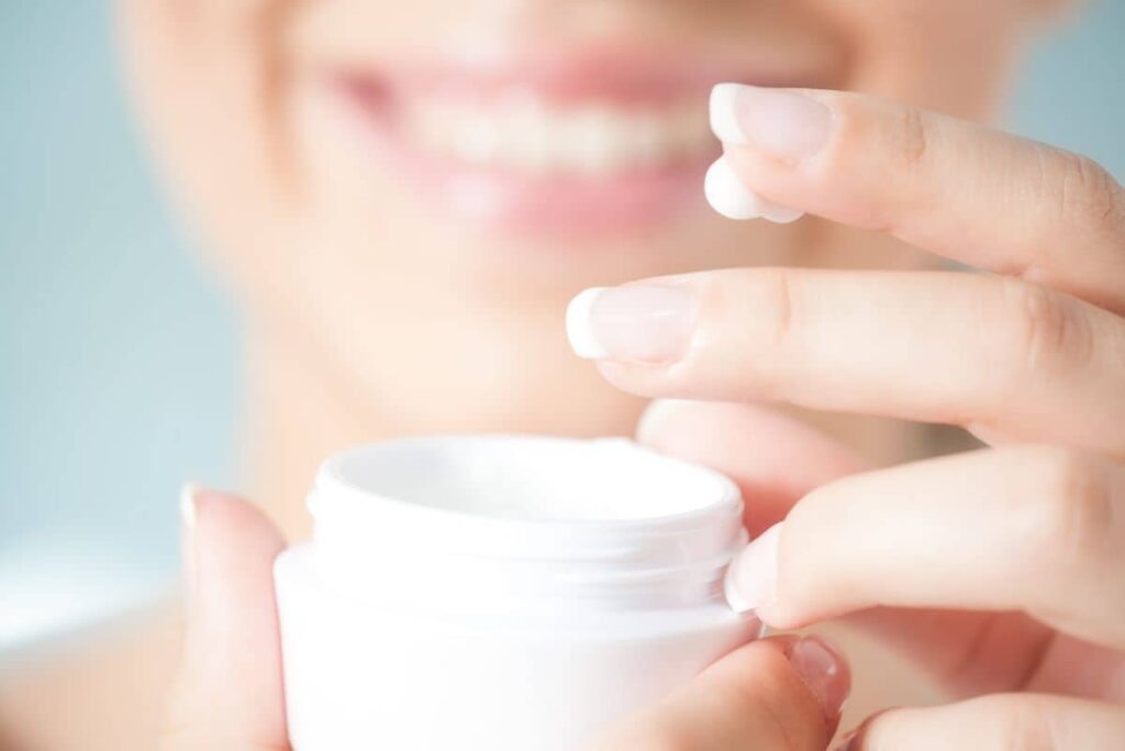 Woman applying topical cream with a smile, symbolizing proper at-home care for facelift scar healing.