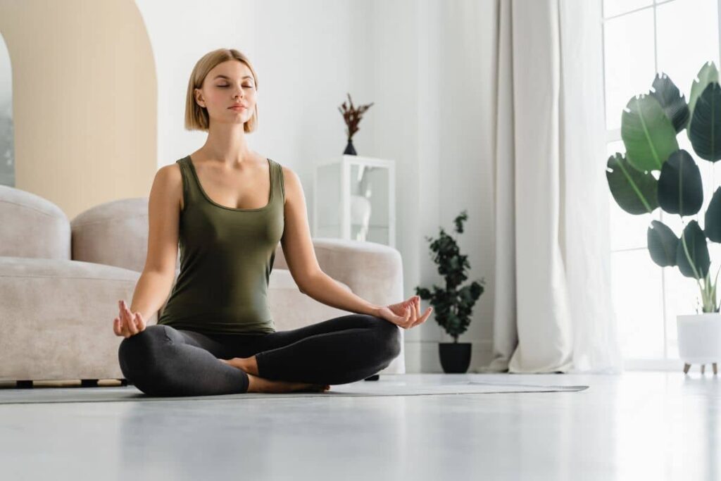 Woman meditating in a bright room to reduce stress and promote wellness before undergoing cosmetic surgery.