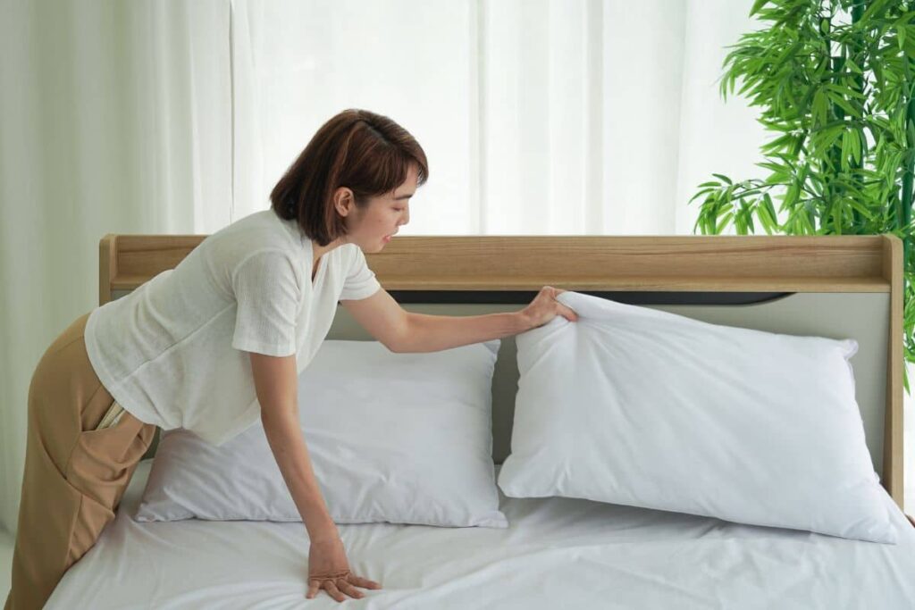 Woman arranging pillows on a bed to create an elevated and supportive sleeping setup for facelift surgery recovery.