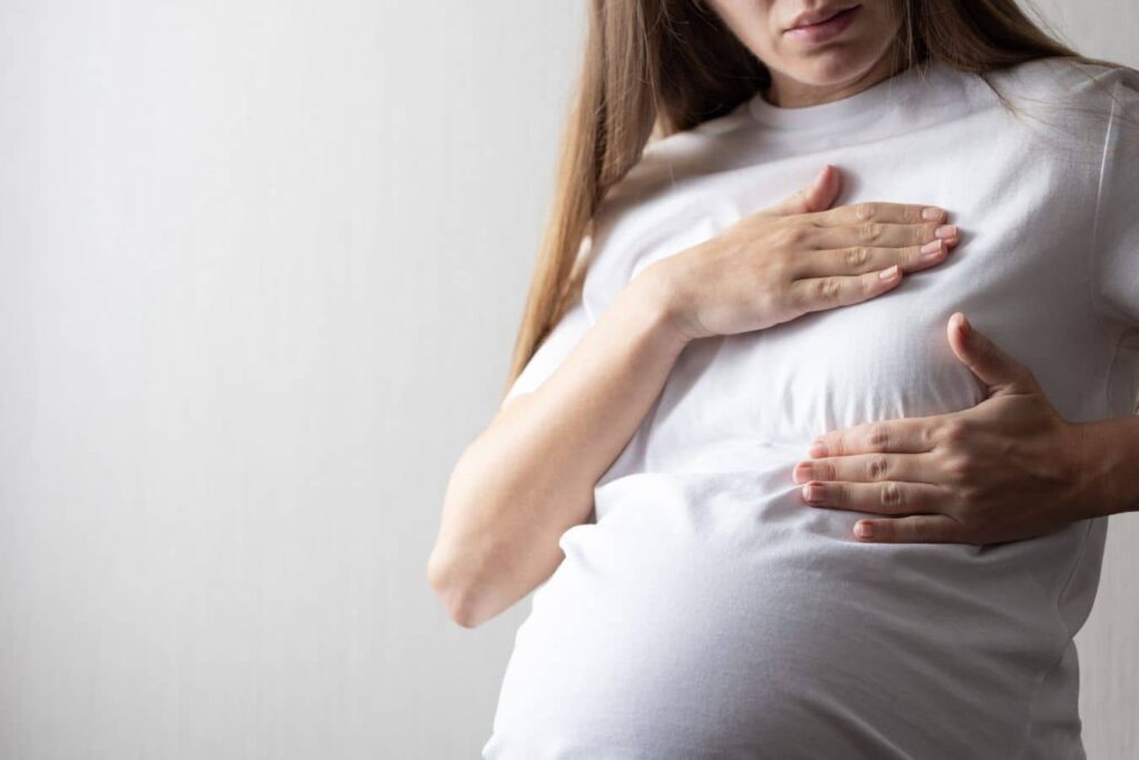Pregnant woman touching her chest, representing how pregnancy may affect breast augmentation results and breast shape.